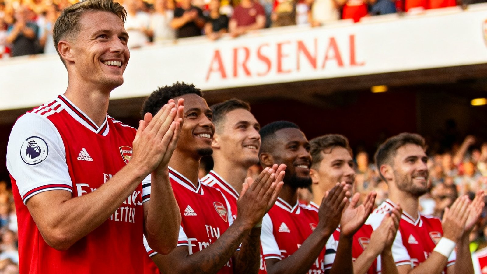 英超联赛阿森纳队客场2-0取胜后全队在客队球迷区前致谢，球员们身穿红色球衣肩并肩排列的温馨画面。